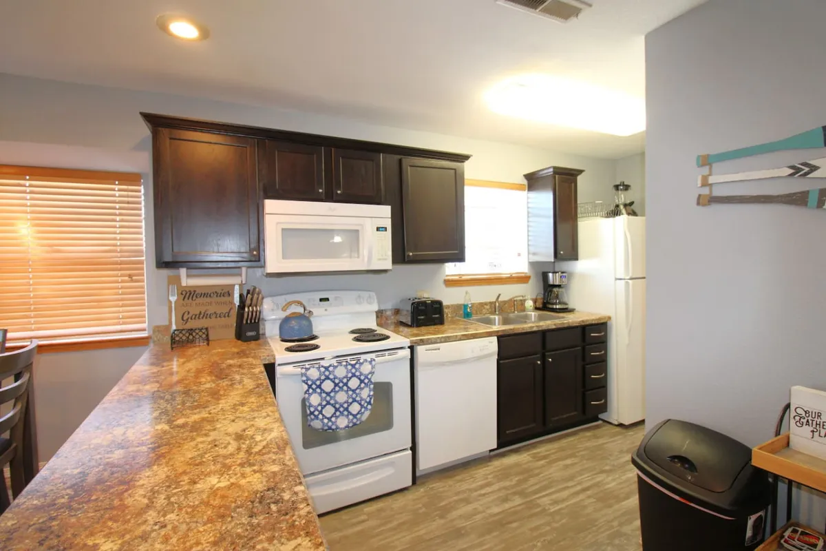 A cozy, well-lit kitchen scene with a focus on the kitchen counter, stove, and sink set beneath a window. The layout provides plenty of room for meal prep and group activities, complemented by natural light pouring through the window.