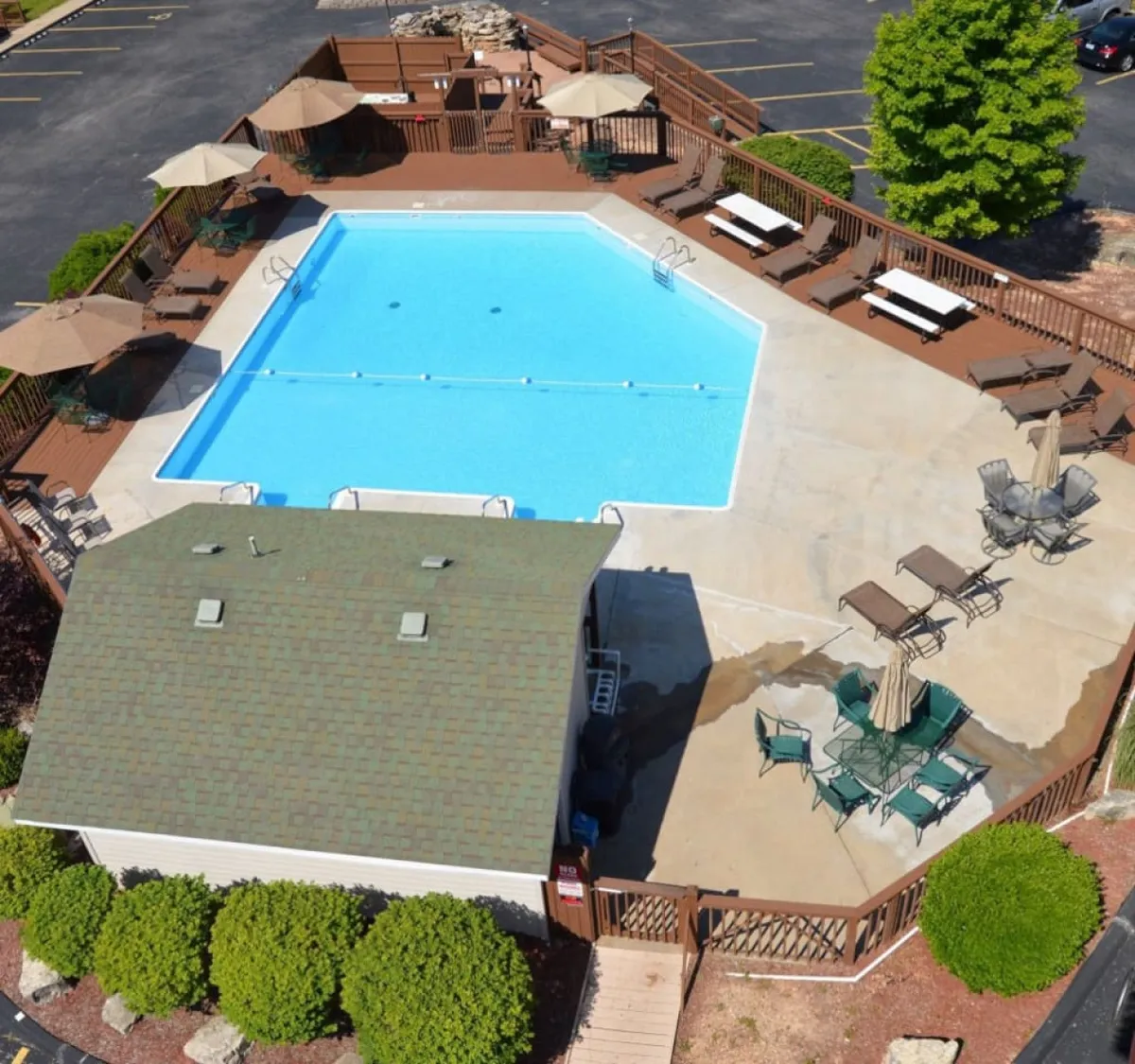 A vibrant outdoor pool scene with a large swimming pool at the center, surrounded by a spacious deck, plenty of lounge chairs, umbrellas, and lush landscaped greenery. Families and friends are relaxing by the pool, kids are playing in the water, and the area exudes a cheerful, resort-like atmosphere.