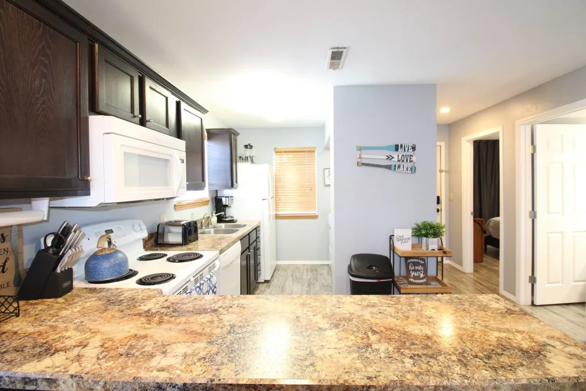 A bright kitchen interior featuring a sleek granite countertop, modern stainless appliances, and decorative wall art. The scene shows ample workspace ideal for meal preparation, with inviting touches for gatherings and group cooking.