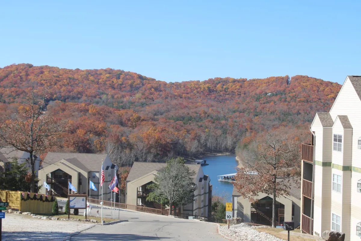 The image showcases a tranquil view of colorful autumn foliage reflected in a calm lake, with charming residential buildings nestled along the shoreline. The scene evokes a sense of peaceful retreat and invites outdoor adventures like boating, hiking, and relaxing by the water.