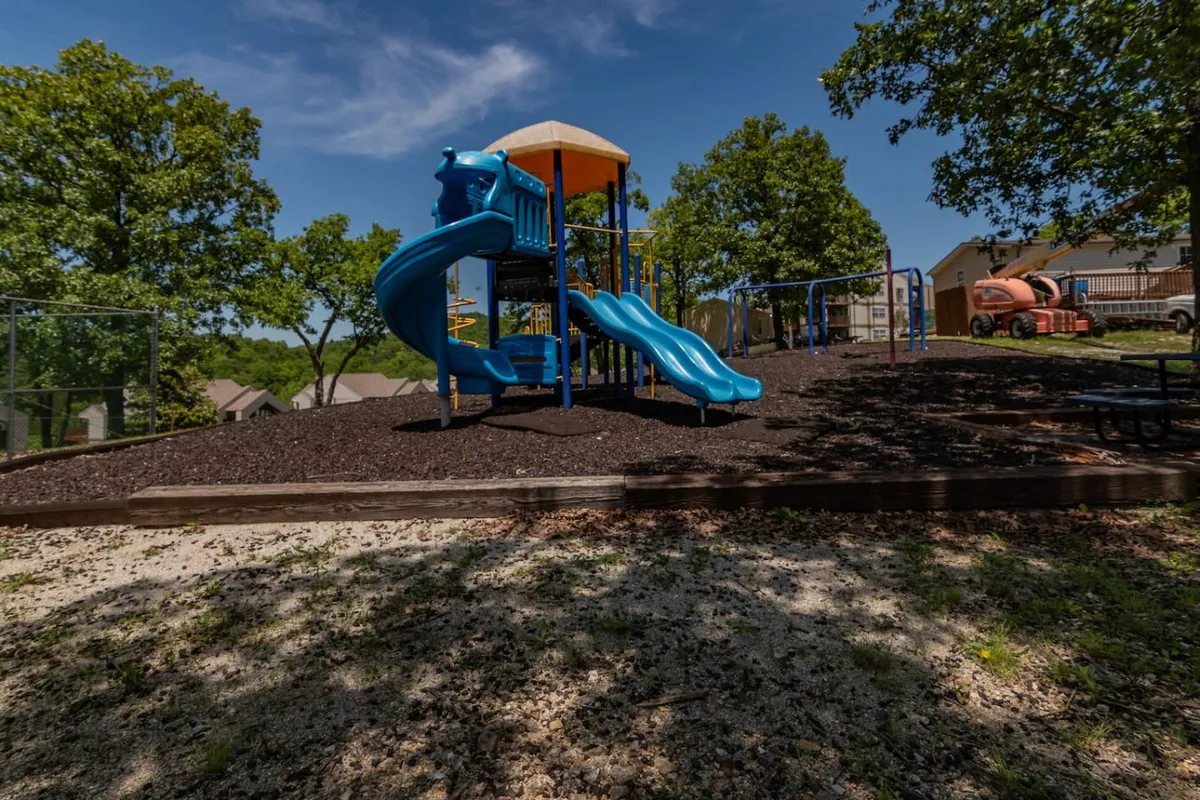 A colorful playground with slides and a swing set, surrounded by families and children playing joyfully. Picnic tables in the background suggest opportunities for outdoor gatherings and birthday parties.